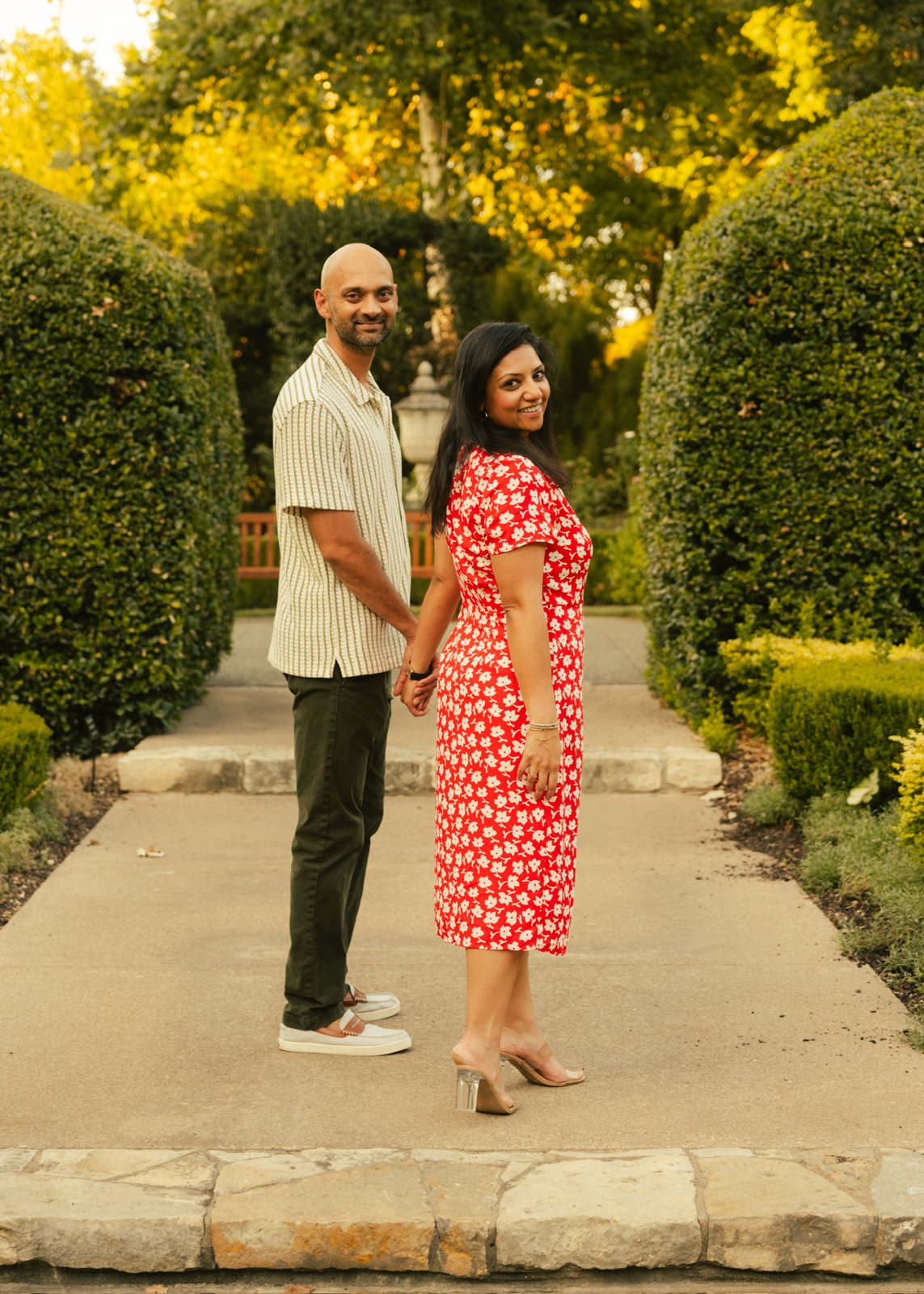 Krishna and Harsh holding hands on a garden path, looking back and smiling